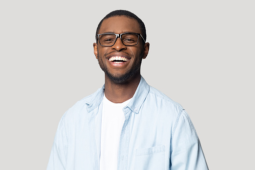 Joyful happy african american young man in eyeglasses portrait. Isolated on grey studio background smiling millennial black guy looking at camera, laughing, having fun, posing for photo head shot.