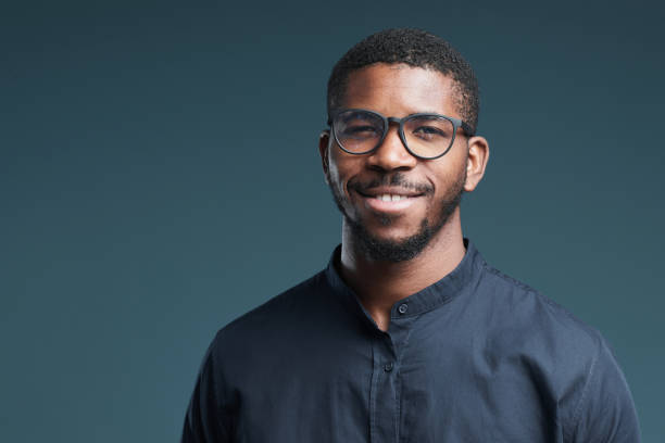 Portrait of handsome African-American man wearing glasses and looking at camera smiling while posing against deep blue background, copy space